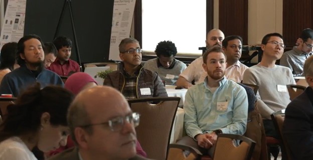 People with name tags sitting in chairs at a conference listening to a speaker